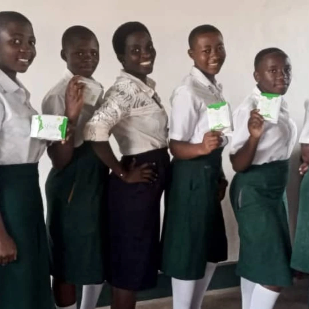 Students and a teacher displaying reusable menstrual pad products in a classroom.