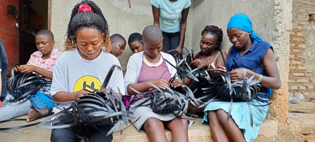 Teenage girls work on black woven baskets during training.
