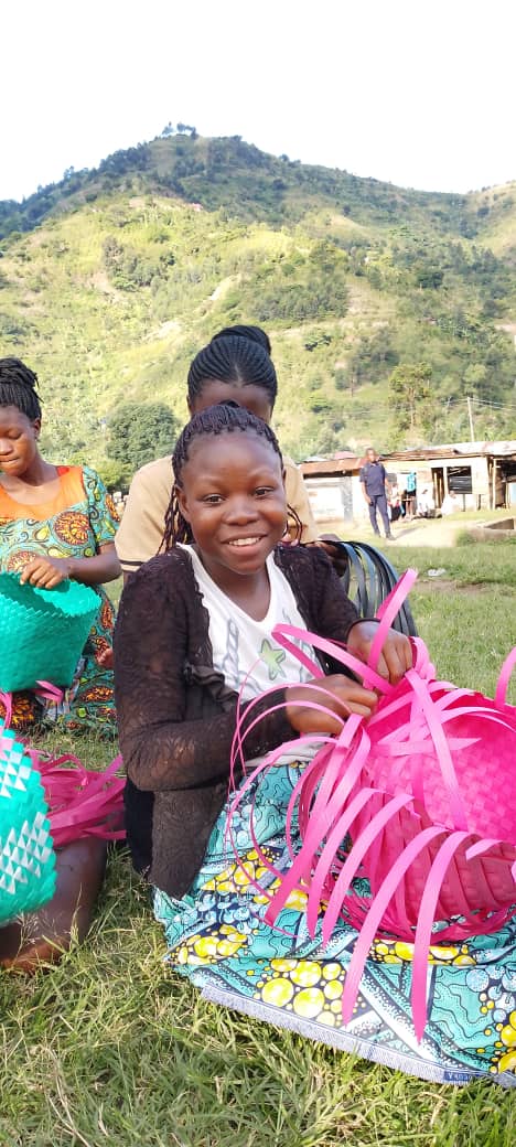 A young woman weaves a basket with mountains in the background.