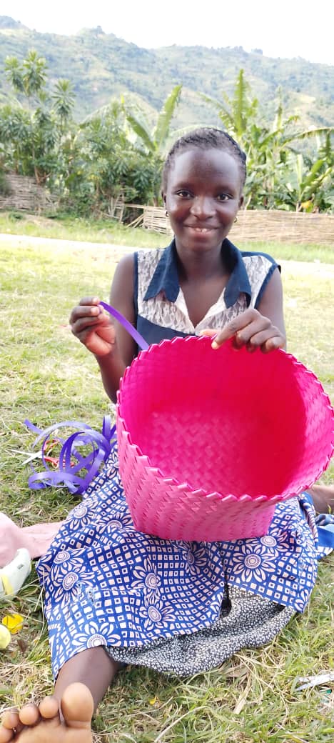 A young woman works on a pink woven basket during skills practice.